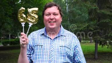 大个子拿着金色气球，把65号的号码放在户外。 65周年庆祝晚会